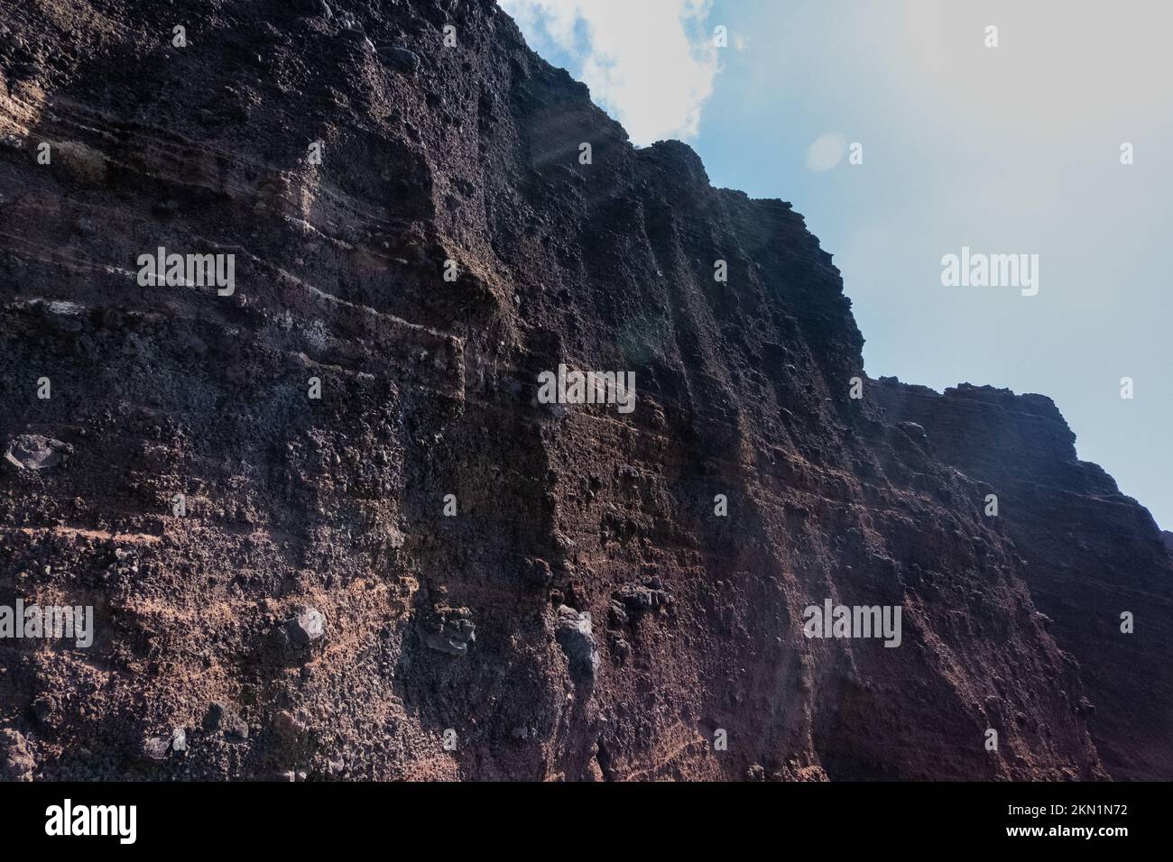 Red beach volcanic stone wall with cloudy sky Stock Photo