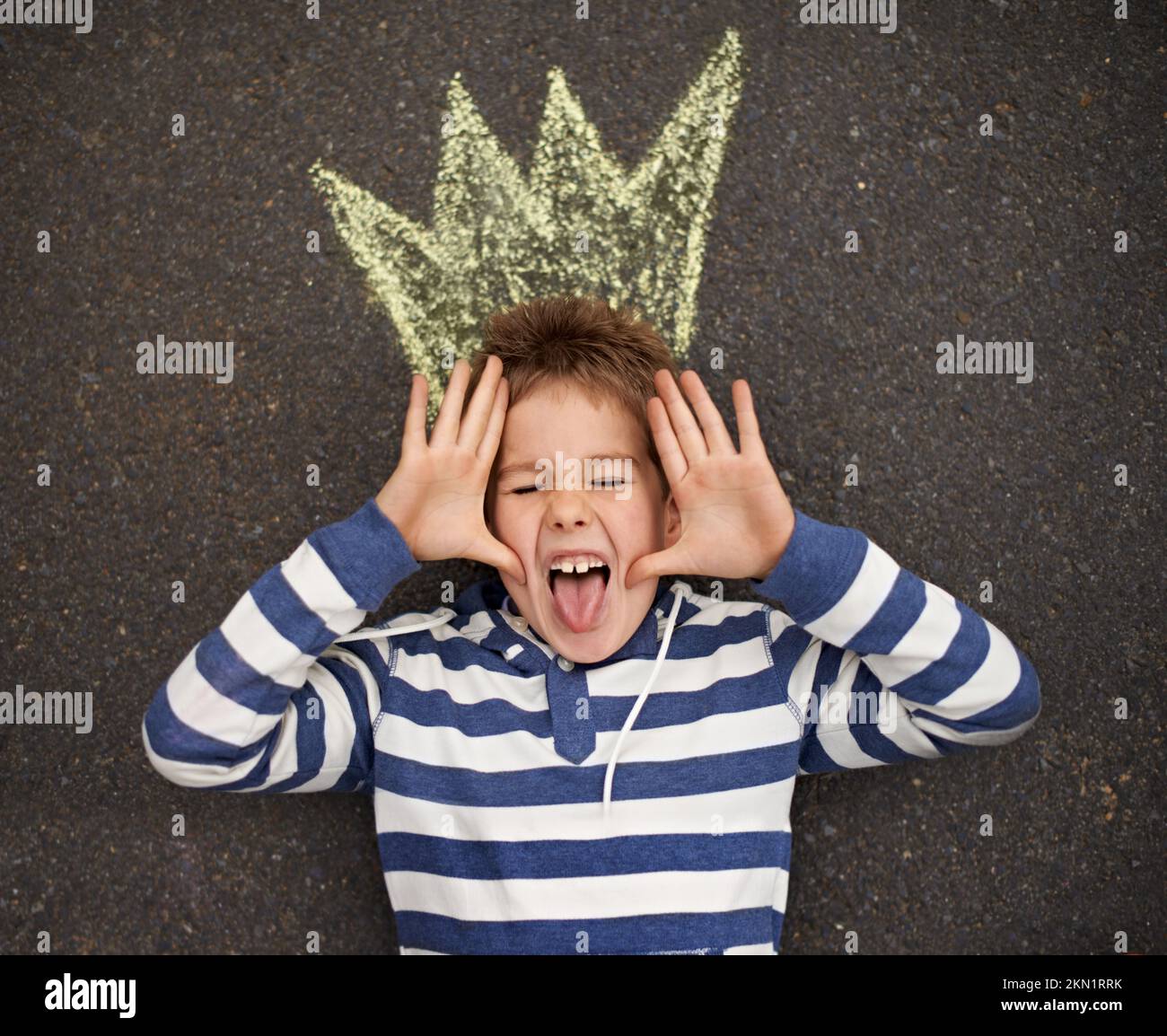 Being a silly billy. Top view shot of a young boy lying on the ground and pulling faces at the camera. Stock Photo