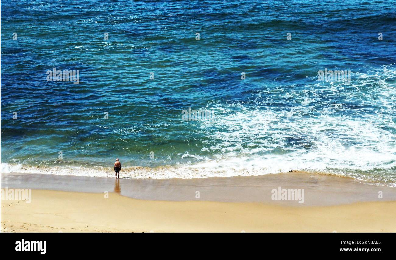 A lone older man stands at the surf edge on Newcastle Beach Stock Photo
