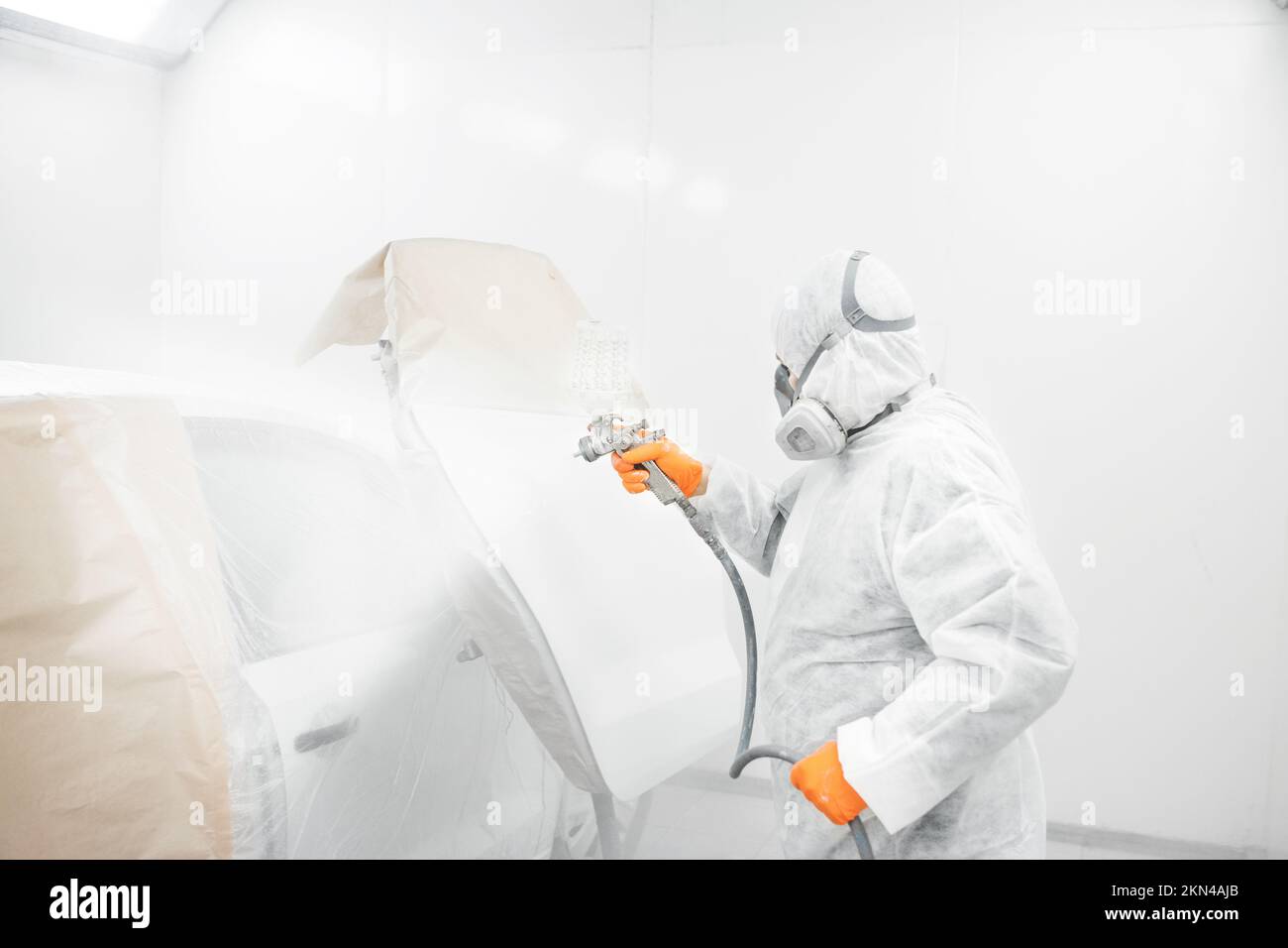 Professional male car painter is painting in garage by airbrush. Worker