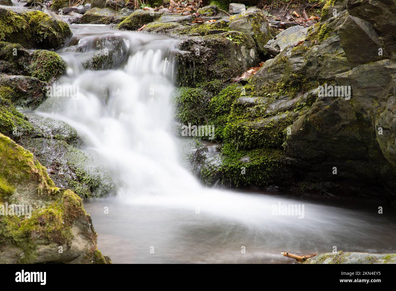 A long exposure of a scenic waterfall flowing down rugged rocks covered ...