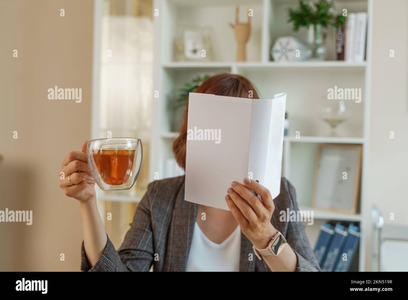 Portrait of a girl holding an open book to her face in one hand and a ...