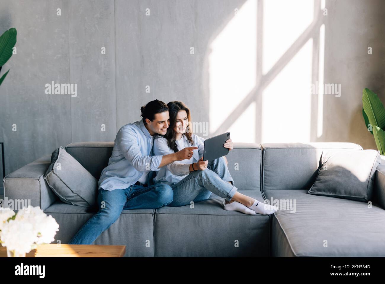 Happy young couple using computer tablet together, sitting on cozy couch at home, smiling beautiful woman and man looking at screen, surfing internet, Stock Photo