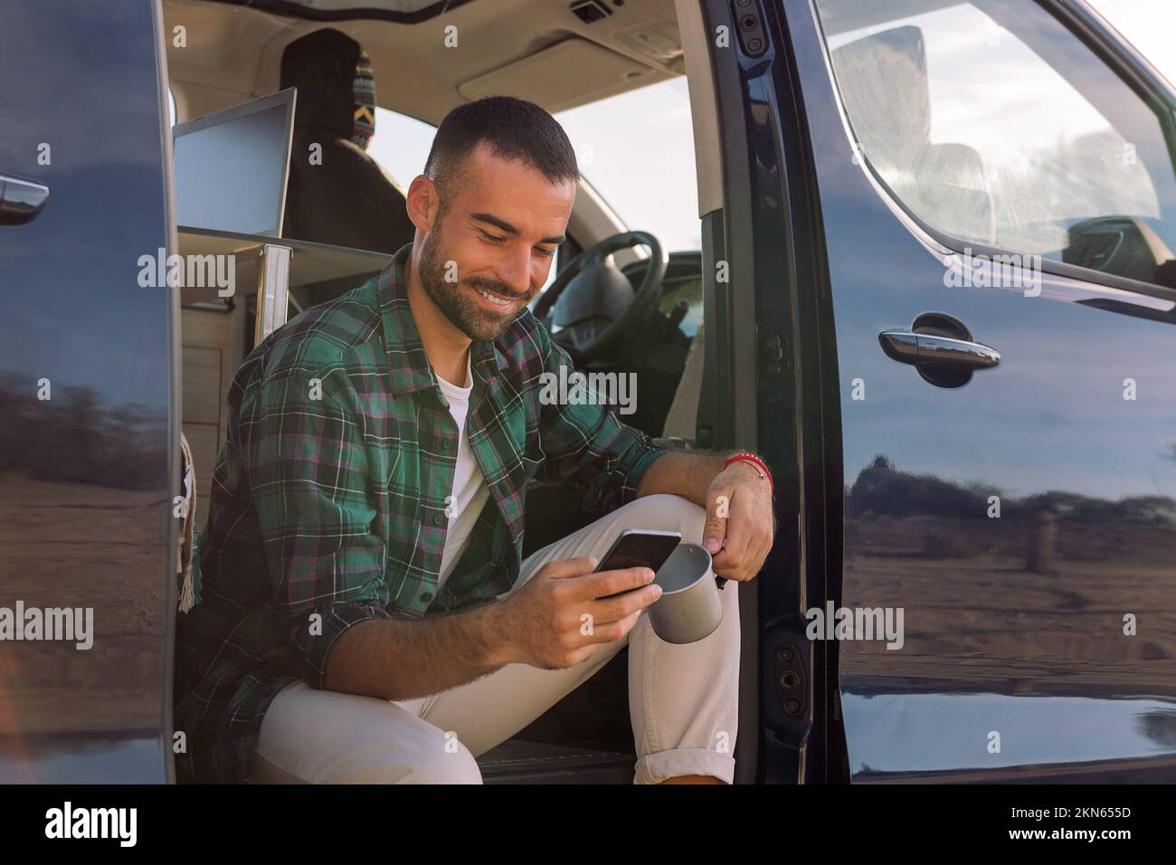 man using his mobile phone sitting on his camper Stock Photo