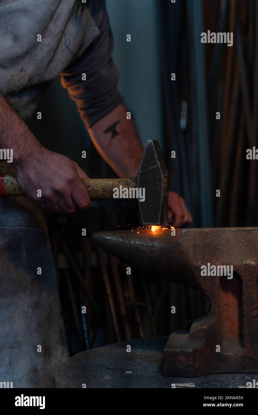 A vertical closeup of a blacksmith forging a tool by heating metal and working with hammer in a smithy Stock Photo