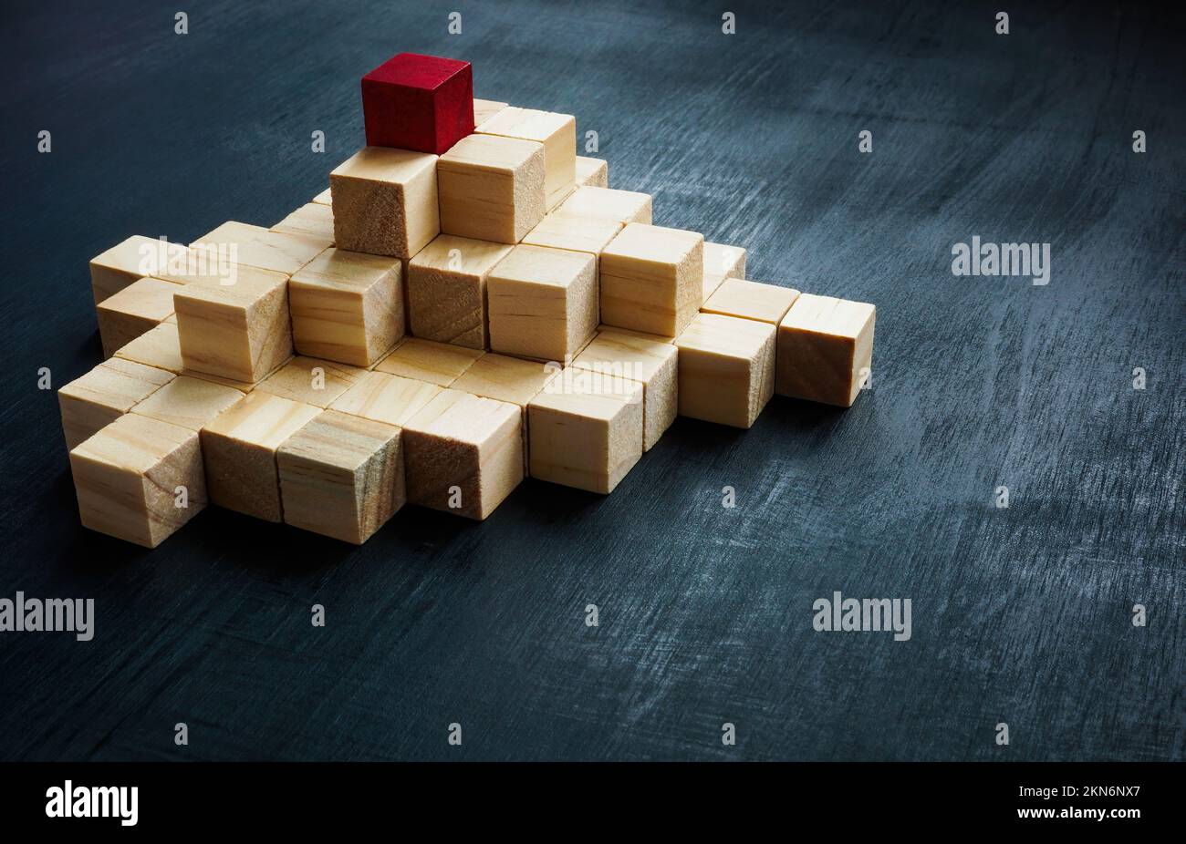 Pyramid from wooden blocks and red one on the top. Leadership concept ...