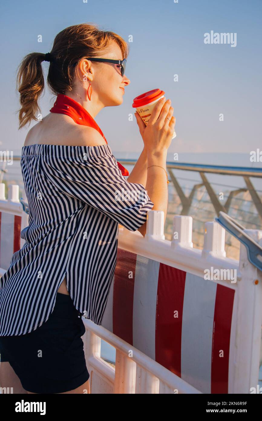 Beautiful girl with coffee cup in morning light. Pretty young woman with sunglasses at the street. Catch the moment. Good vibes concept. Summer girl. Stock Photo