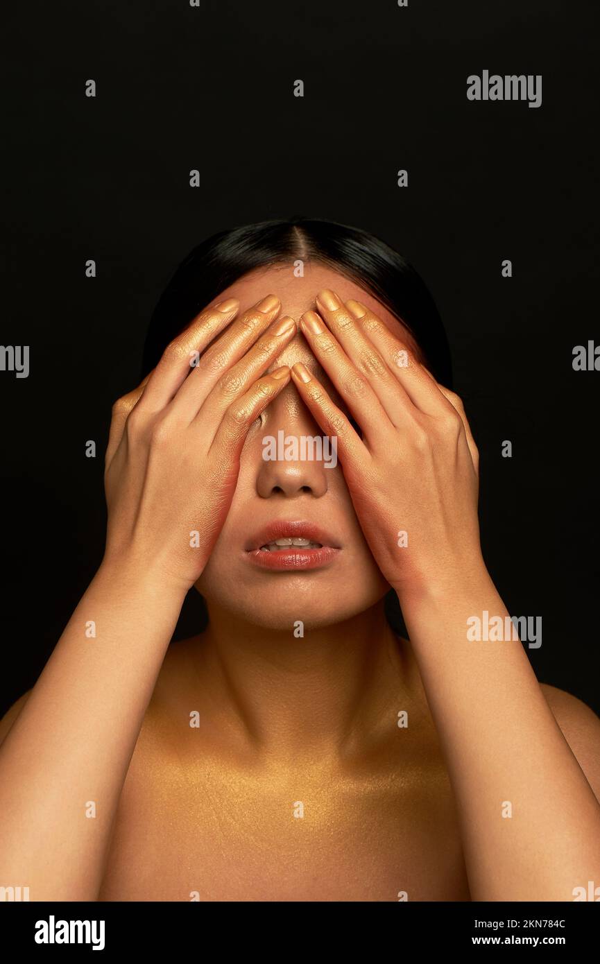 I don't see the evil. An Asian girl on a black background in a photo studio. Gold. Stock Photo