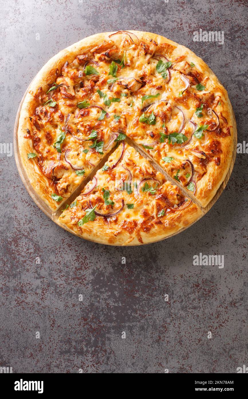 American California pizza with chicken, barbecue sauce, cheese and onions close-up on a wooden board on the table. Vertical top view from above Stock Photo