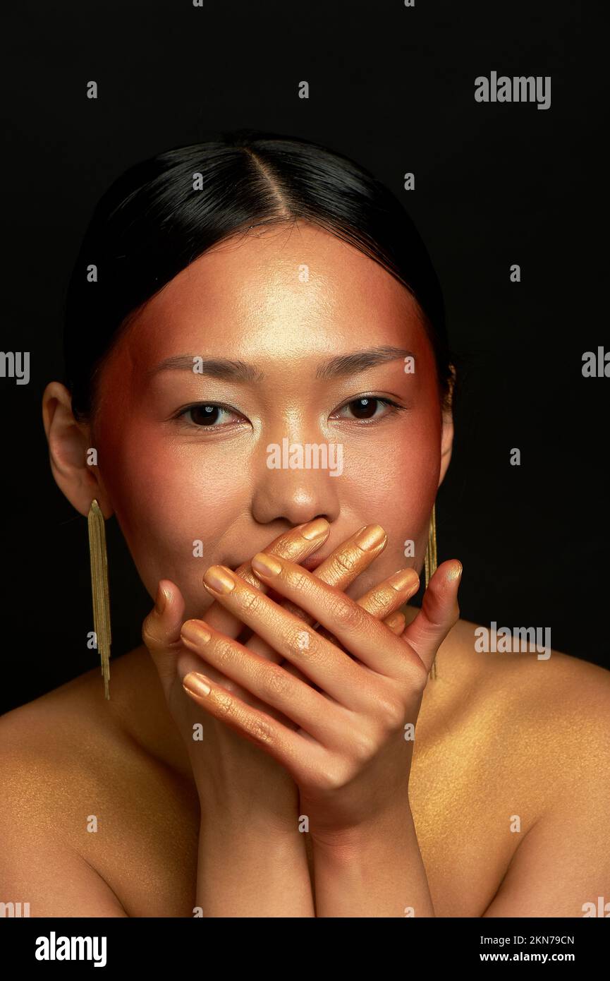 An Asian girl on a black background in the studio. Gold. Hides a smile Stock Photo