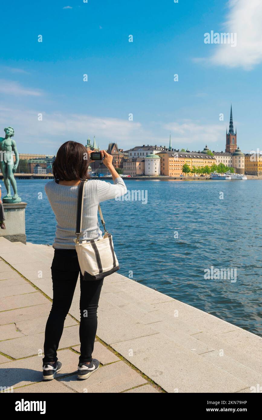 Female travel city, rear view in summer of a young woman taking a photo of Riddarholmen harbour in the central old town district in Stockholm, Sweden Stock Photo