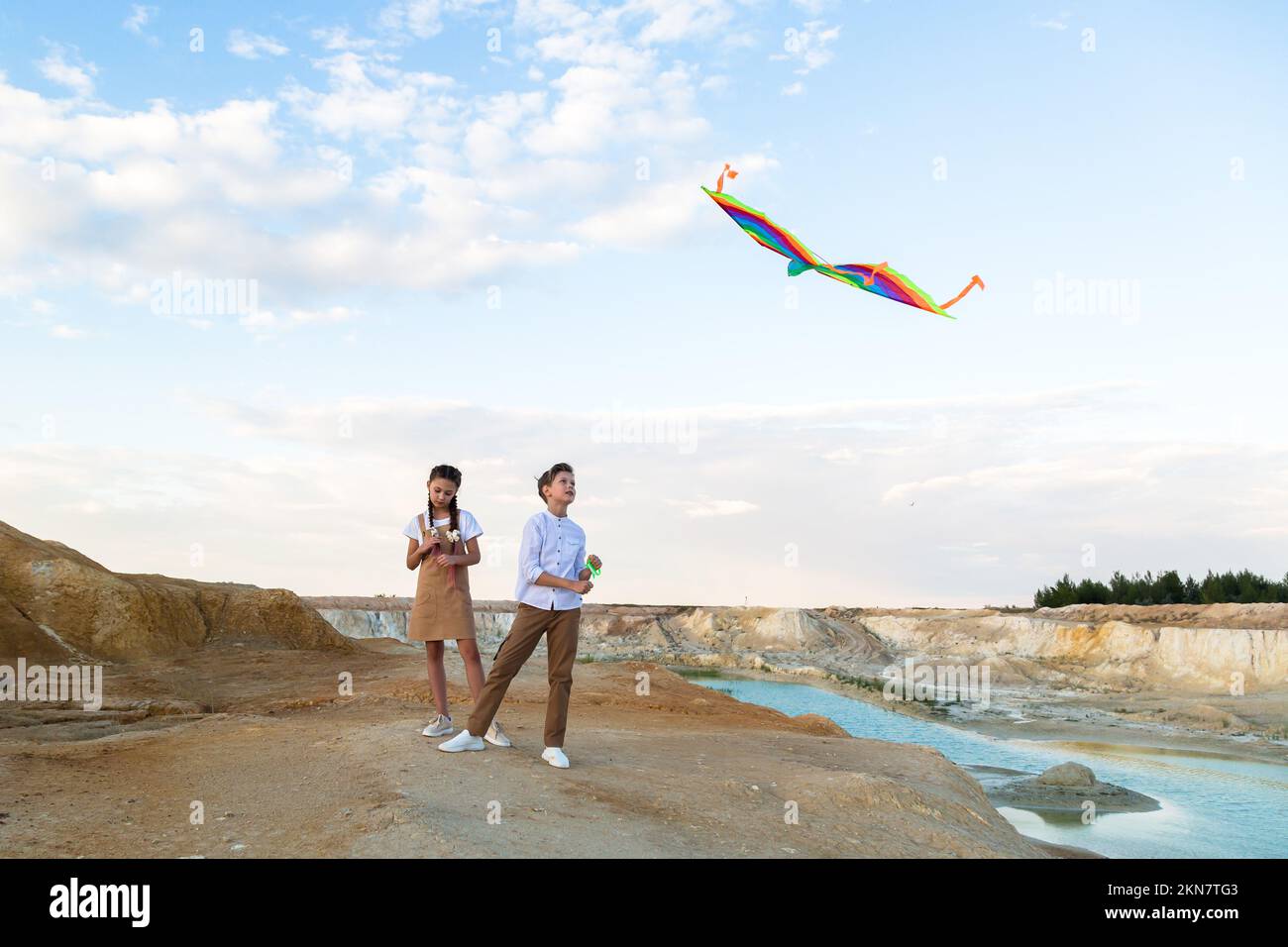 Brother and sister launch a bright big kite into the sky near a flowing river. Stock Photo