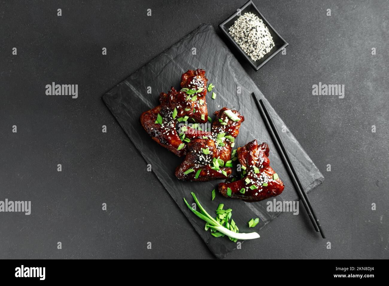 Chicken wings with sesame and green onions. Traditional Asian recipe. Dark background. Top view. Stock Photo