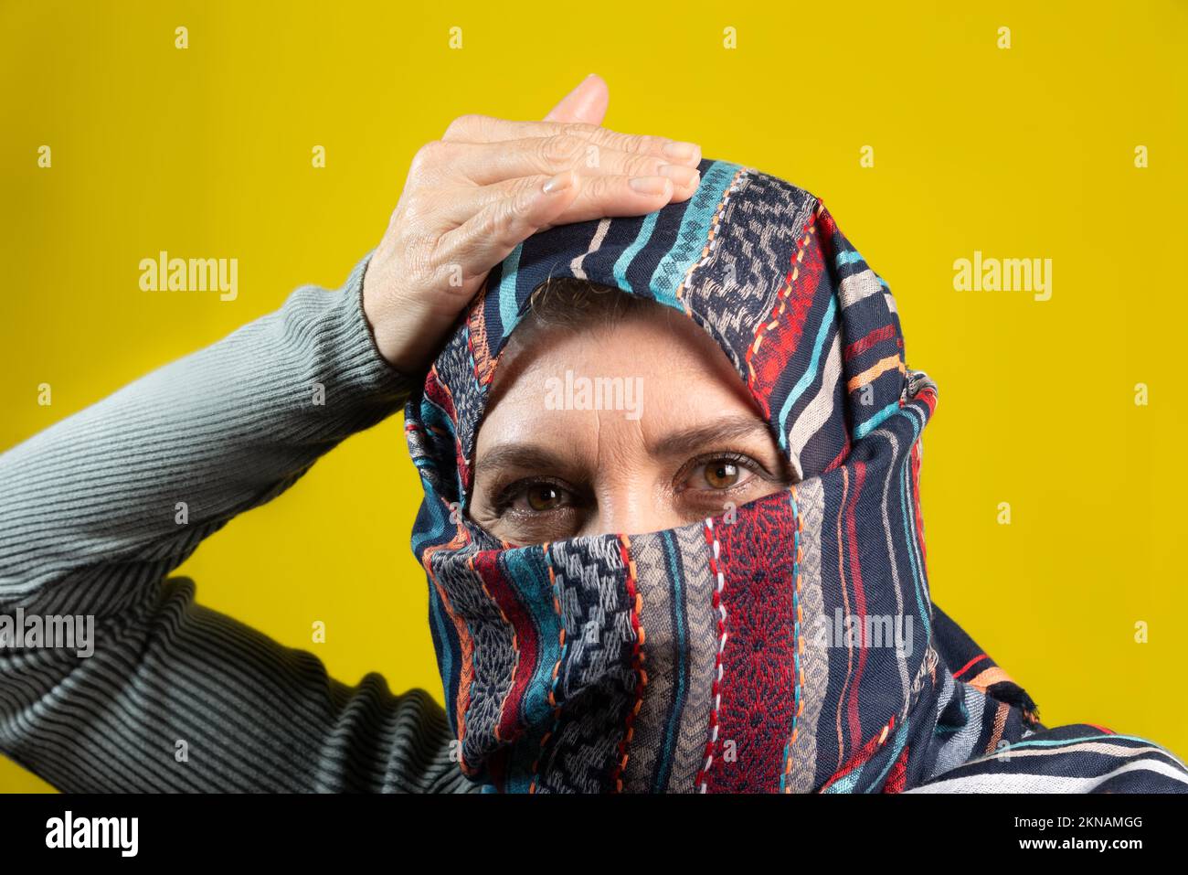 Portrait of woman wearing hijab, looking at camera, with hand on head, isolated on yellow studio background. Stock Photo