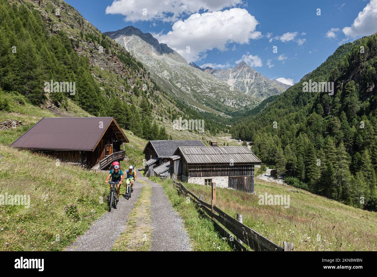 Mountain bikers in front of rustic alpine huts, mountain forests and peaks in the Windach valley, Ötztal Alps, Austria Stock Photo
