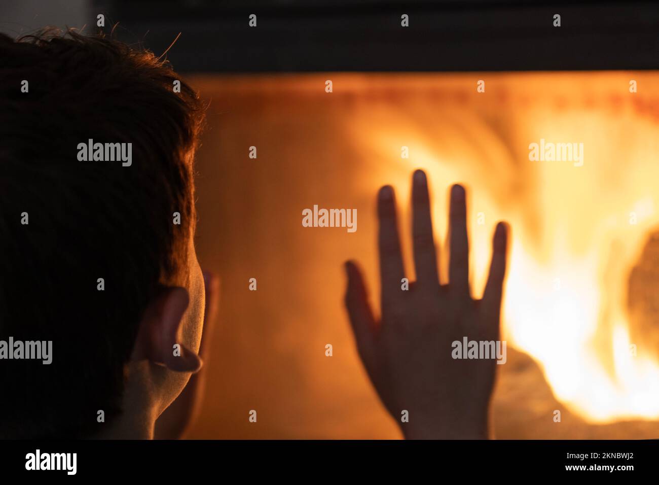Kid warms with fire burning wood at home - No electricity during an energy crisis in Europe causing blackouts Stock Photo