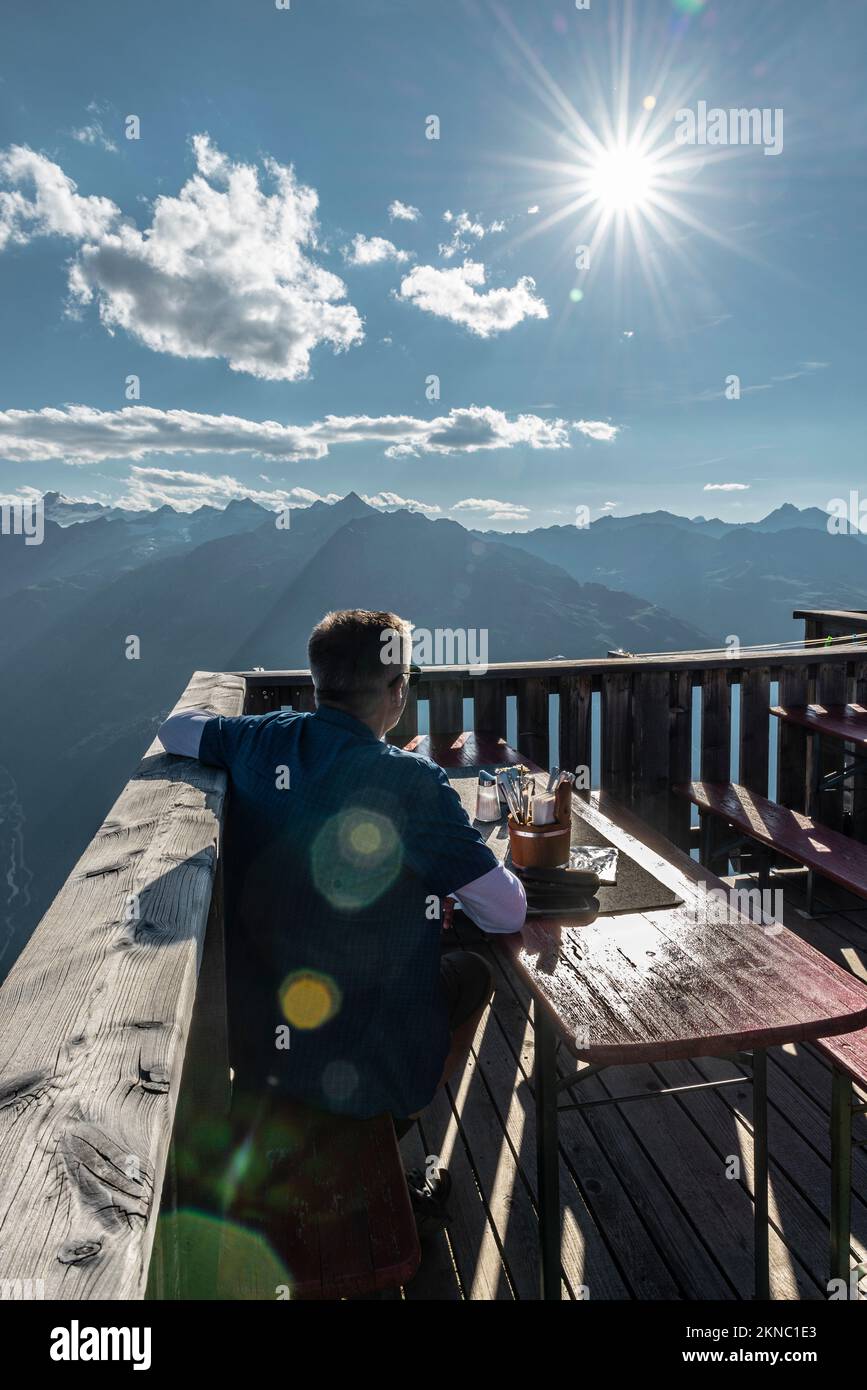 A hiker sits on the terrace at the Brunnenkogelhaus mountan hut and looks at the panorama of the Ötztal Alps and Gurgl Valley, Tyrol, Austria Stock Photo