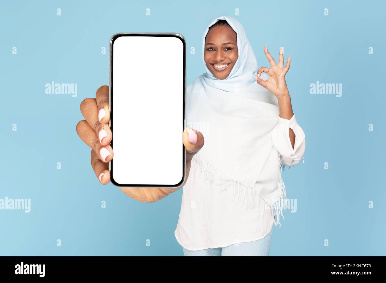 Excited black muslim woman showing phone blank screen and gesturing okay, space for website or app design, mockup Stock Photo