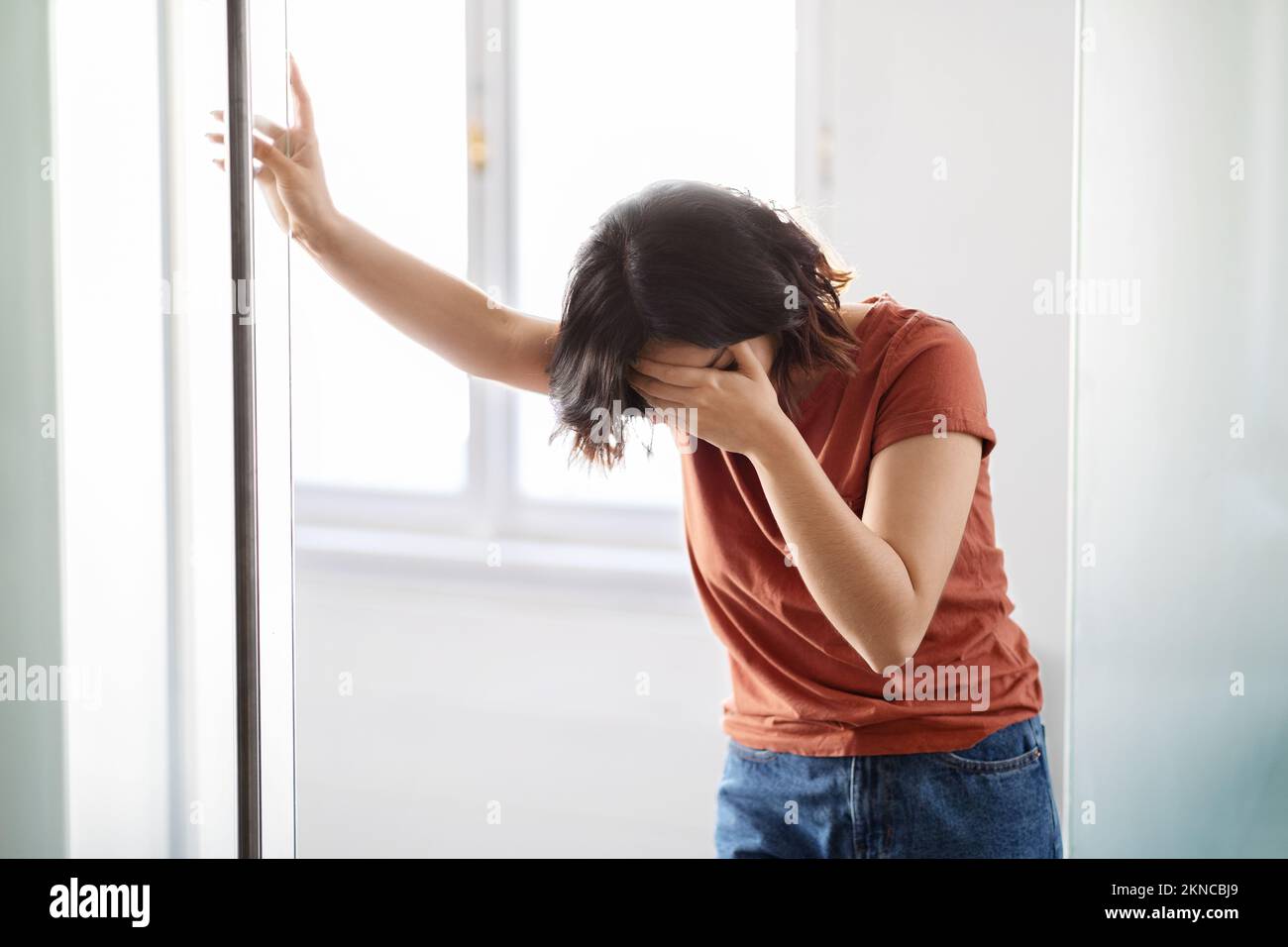 Portrait Of Depressed Young Woman Crying Near Window At Home Stock Photo