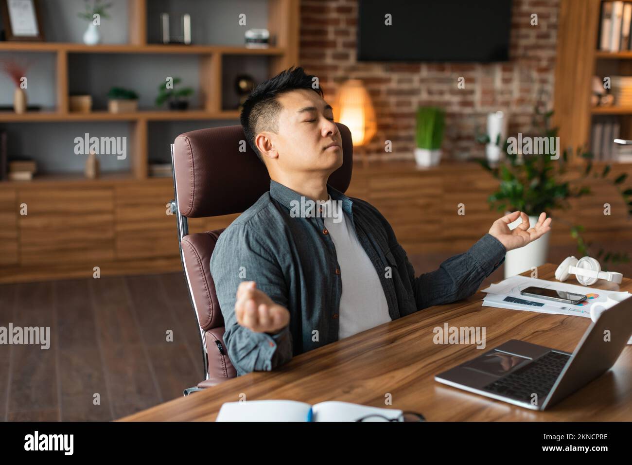 Relaxed adult asian man with closed eyes meditation, rests at table with laptop, enjoys silence and comfort Stock Photo