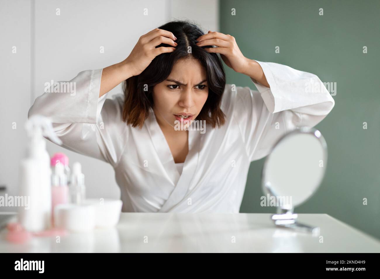 Angry lady in white bathrobe sitting in bedroom, checking hair Stock