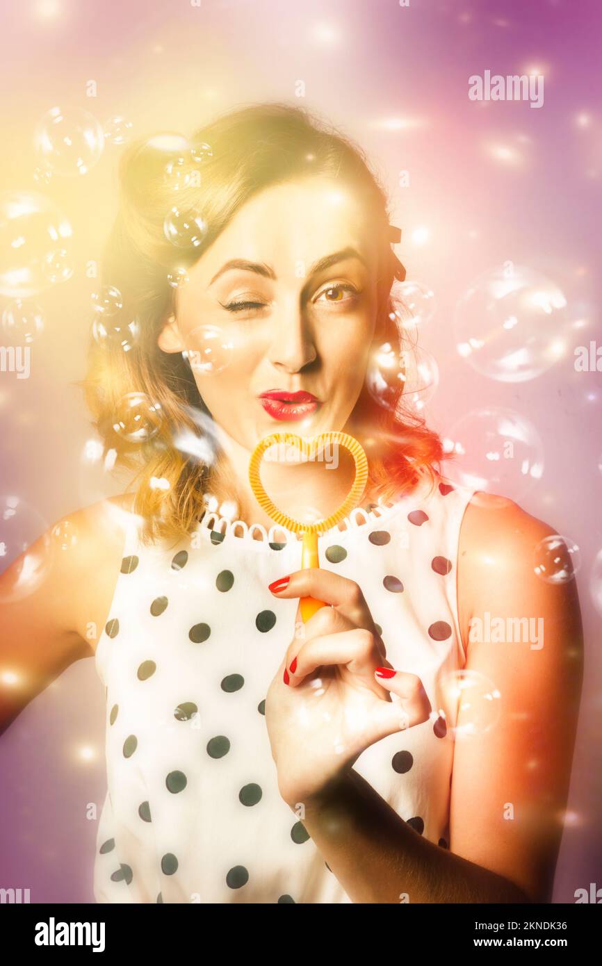 Creative digital artwork of a beautiful retro woman blowing bubbles of love through a heart shaped party blower when giving the gift of romance. Valen Stock Photo