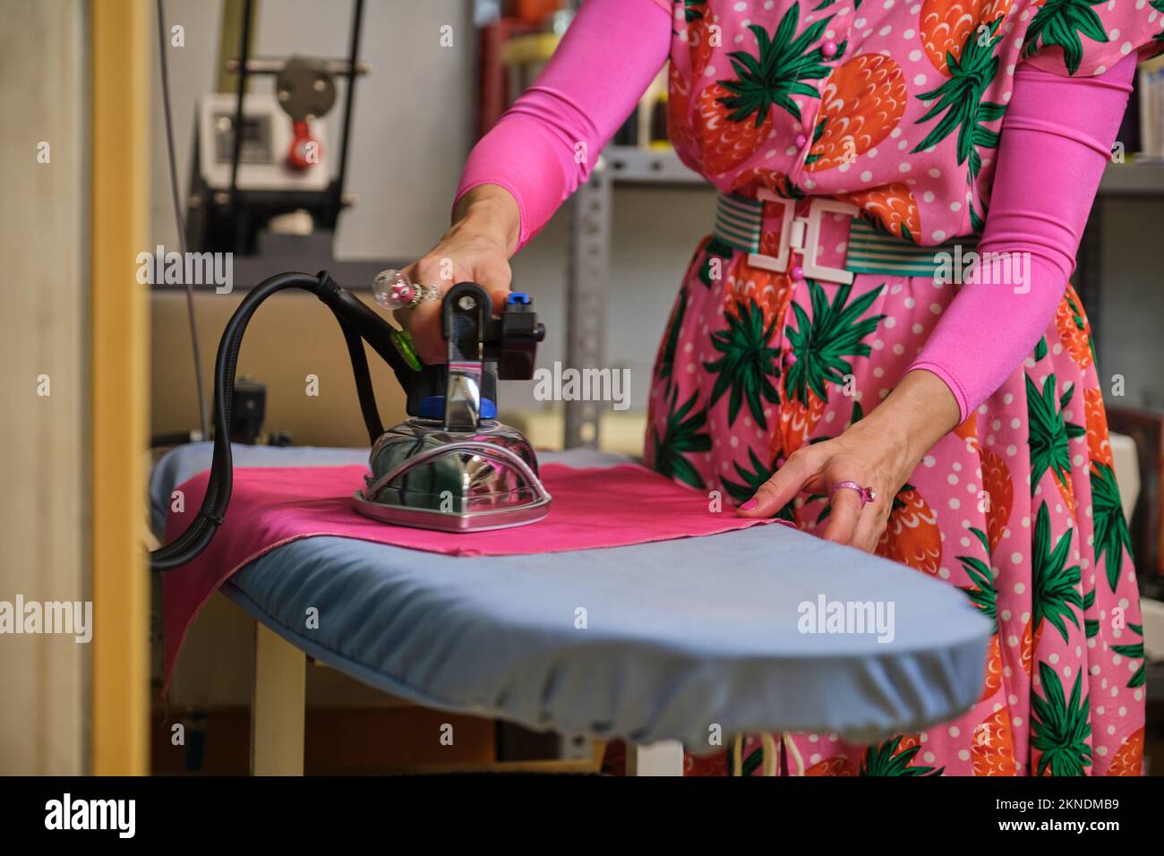 Unrecognizable dressmaker with colorfull clothes ironing fabric. Stock Photo