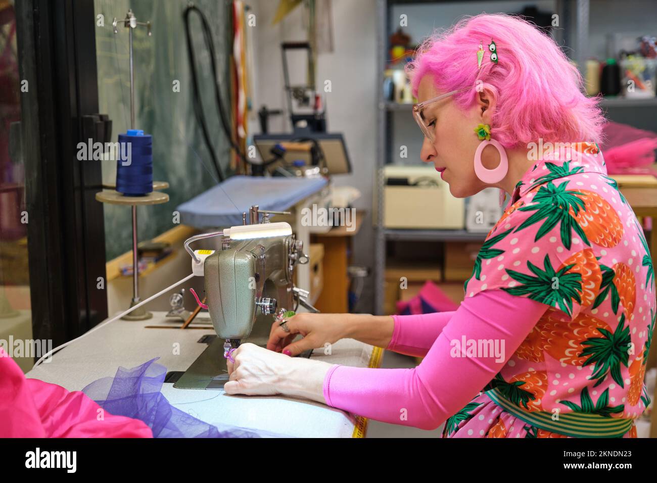 Tailor with pink hair and colorfull clothes threading sewing machine. Stock Photo