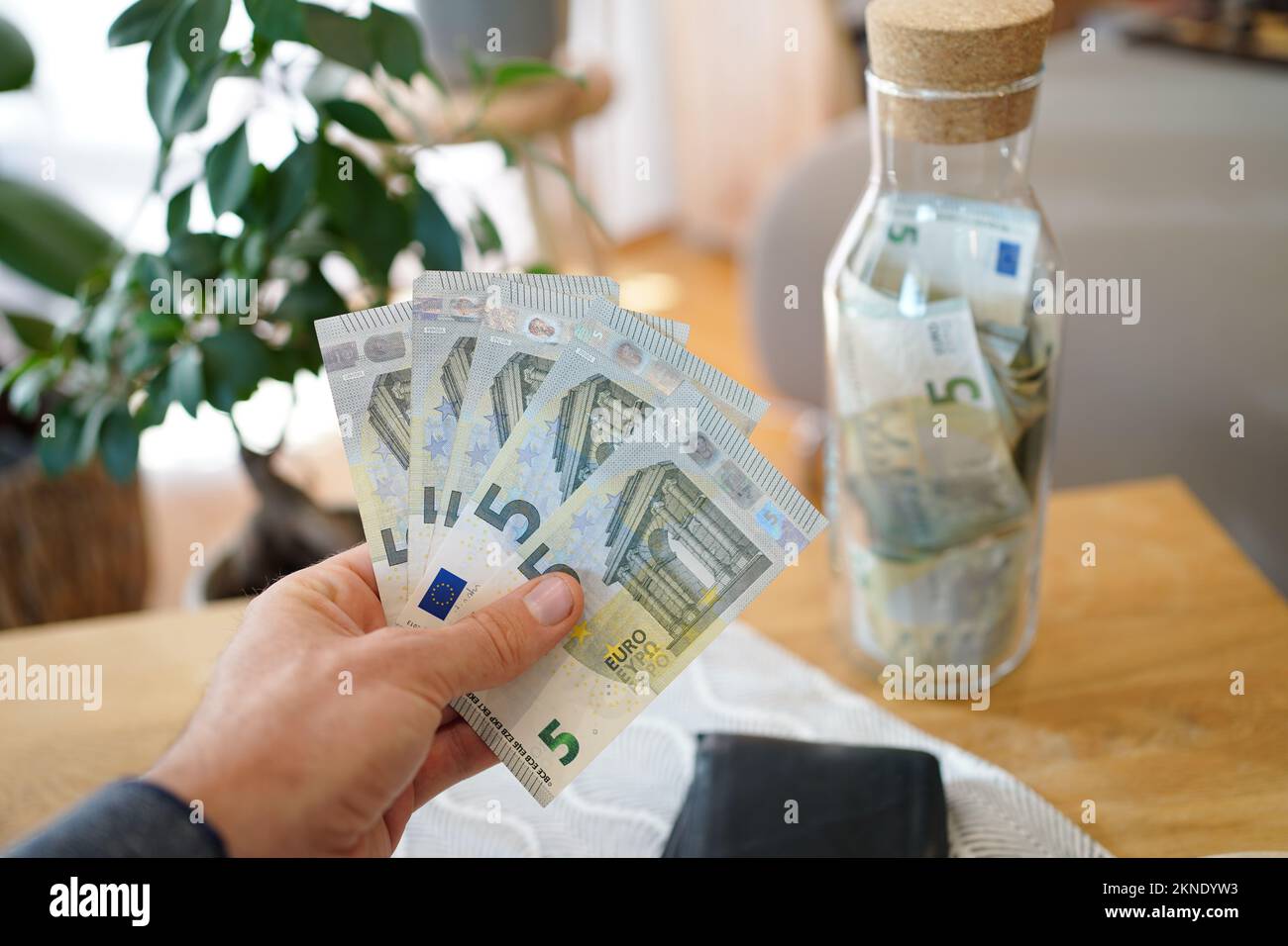 Hand holding five euro notes, saving money in a glass bottle. Stock Photo