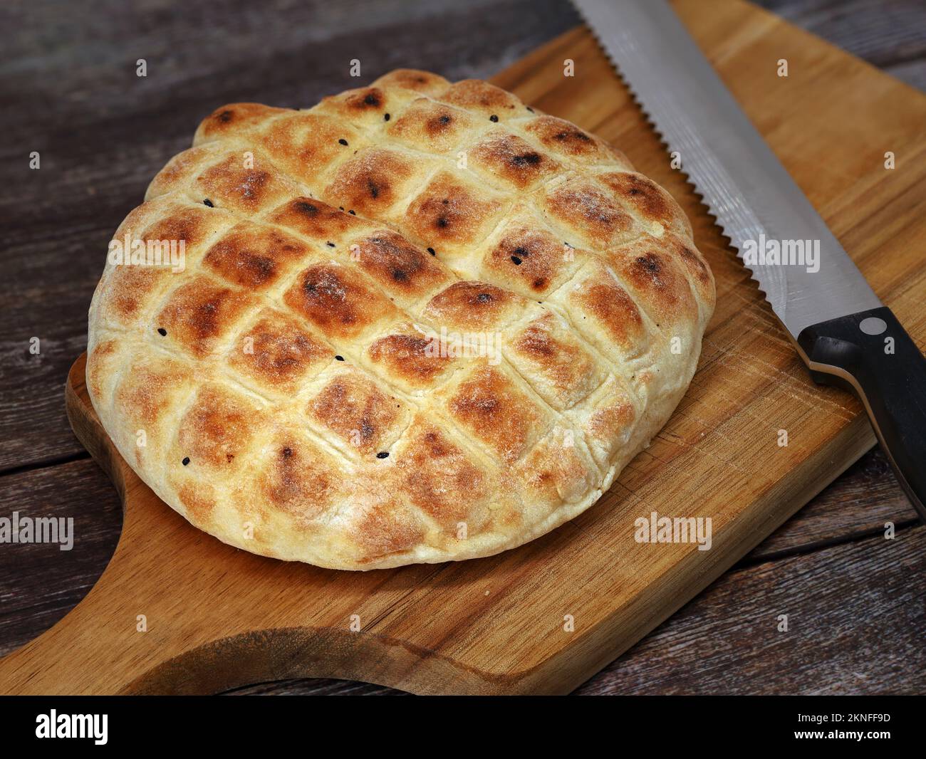 turkish flatbread with black cumin on wooden cutting board with bread knife, round wheat bread for doner kebab Stock Photo