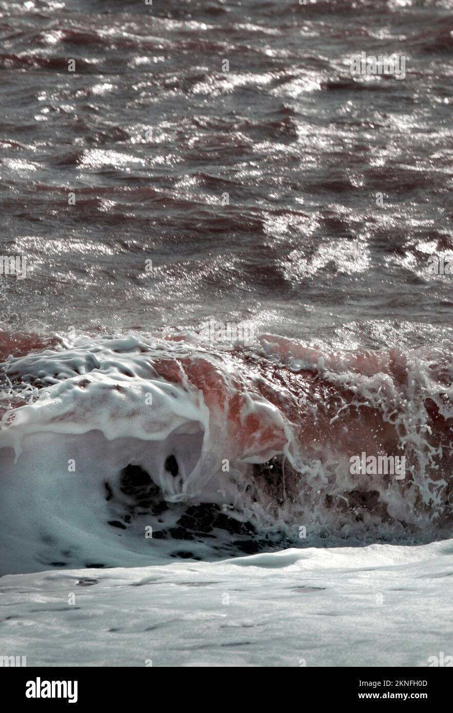 red tinged breaking waves dunwich suffolk england Stock Photo