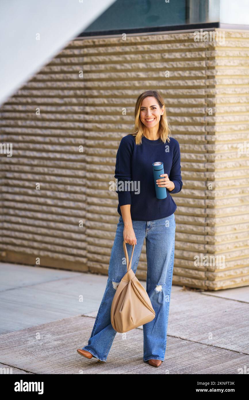Cheerful woman with thermos and bag on street Stock Photo