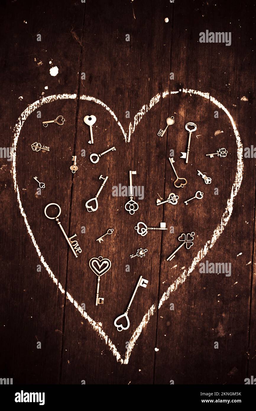 Metal heart keys scattered in chalk heart drawn on wooden background above. Casting love spells Stock Photo