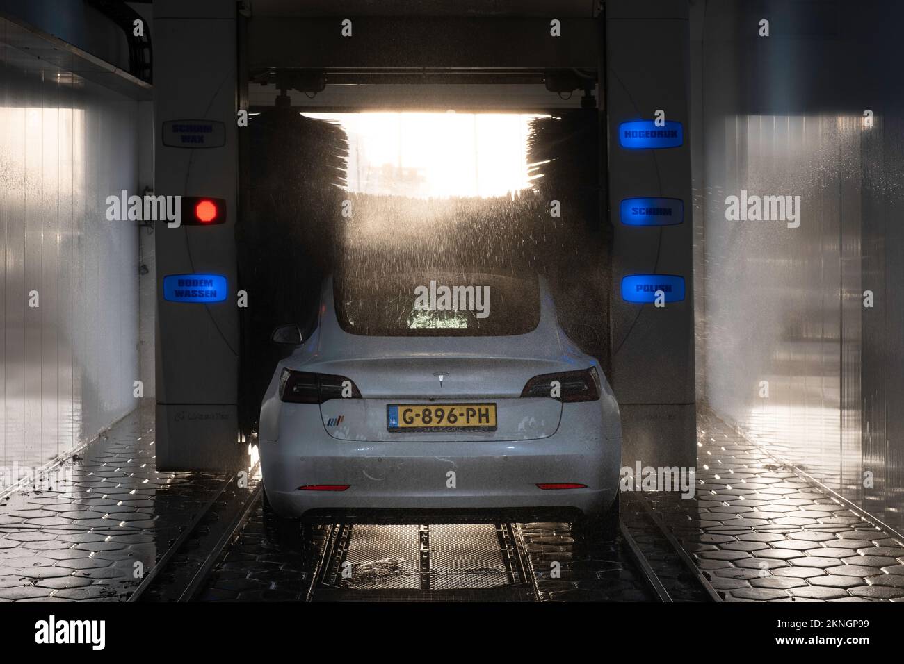 Tesla is washed in a covered automatic car wash with sunlight effect. The water splashes around