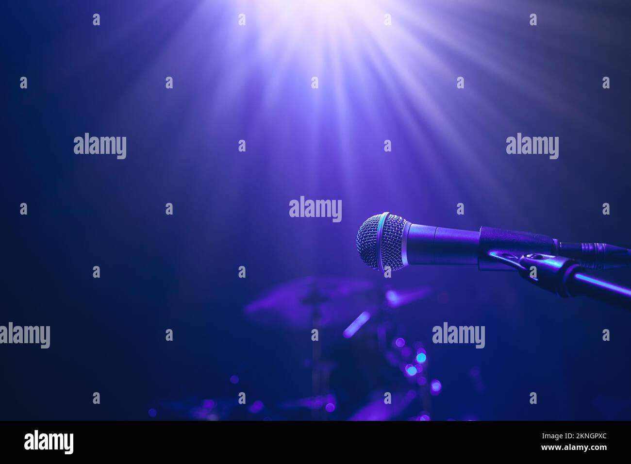 Selective focus on lluminated microphone against drum kit on stage in blue light. Stock Photo