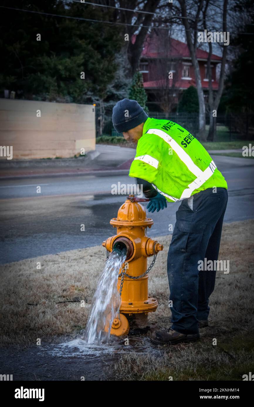 1-29-2019 Tulsa USA Waste and Sewer Worker turning off the water on a yellow fire hydrant near a wet street with two story house in the background acr Stock Photo