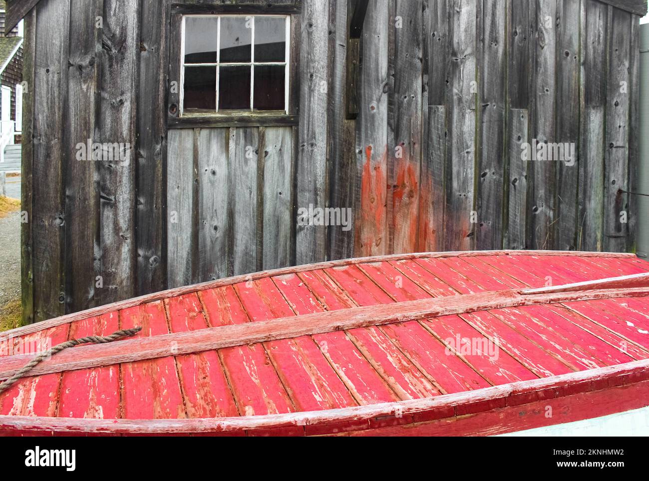 By the sea - Old weathered building behind the bottom of a red painted wooden boat with a rope Stock Photo