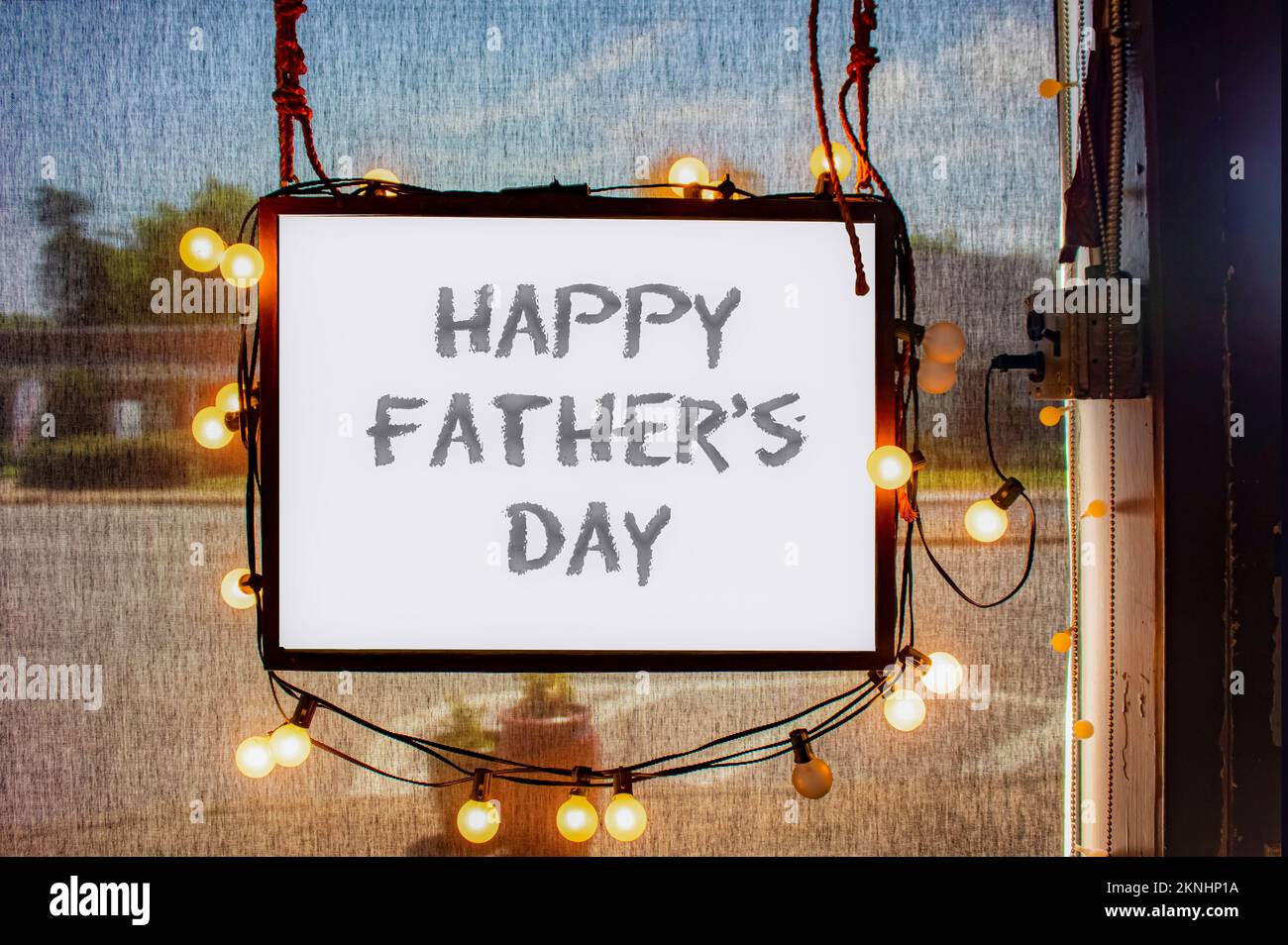 Happy Fathers Day written on hanging sign surrounded by party lights in shop window with semi-transparent dark solar shades behind and dimly viewed ci Stock Photo