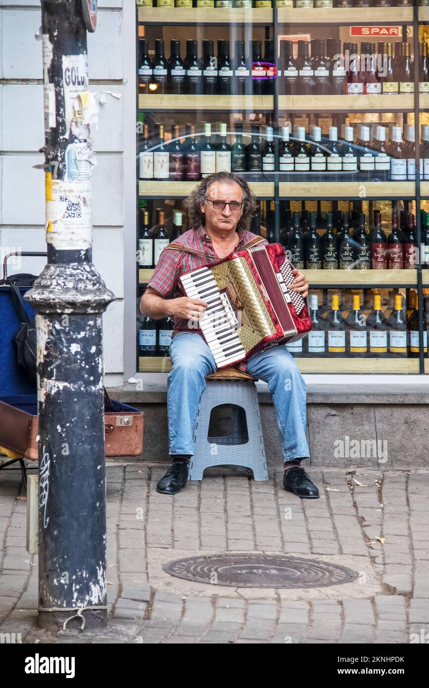 July 15 Tbilisi Georgia - Man sitting on stool in front of wine store playing accordion in Old Town Stock Photo