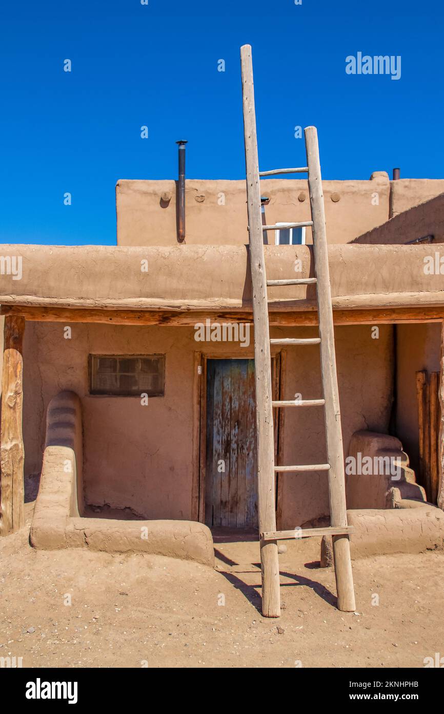 Ladder leading to second story apartments on traditional mud adobe pueblo with porch and old grunge wooden door in American southwest Stock Photo