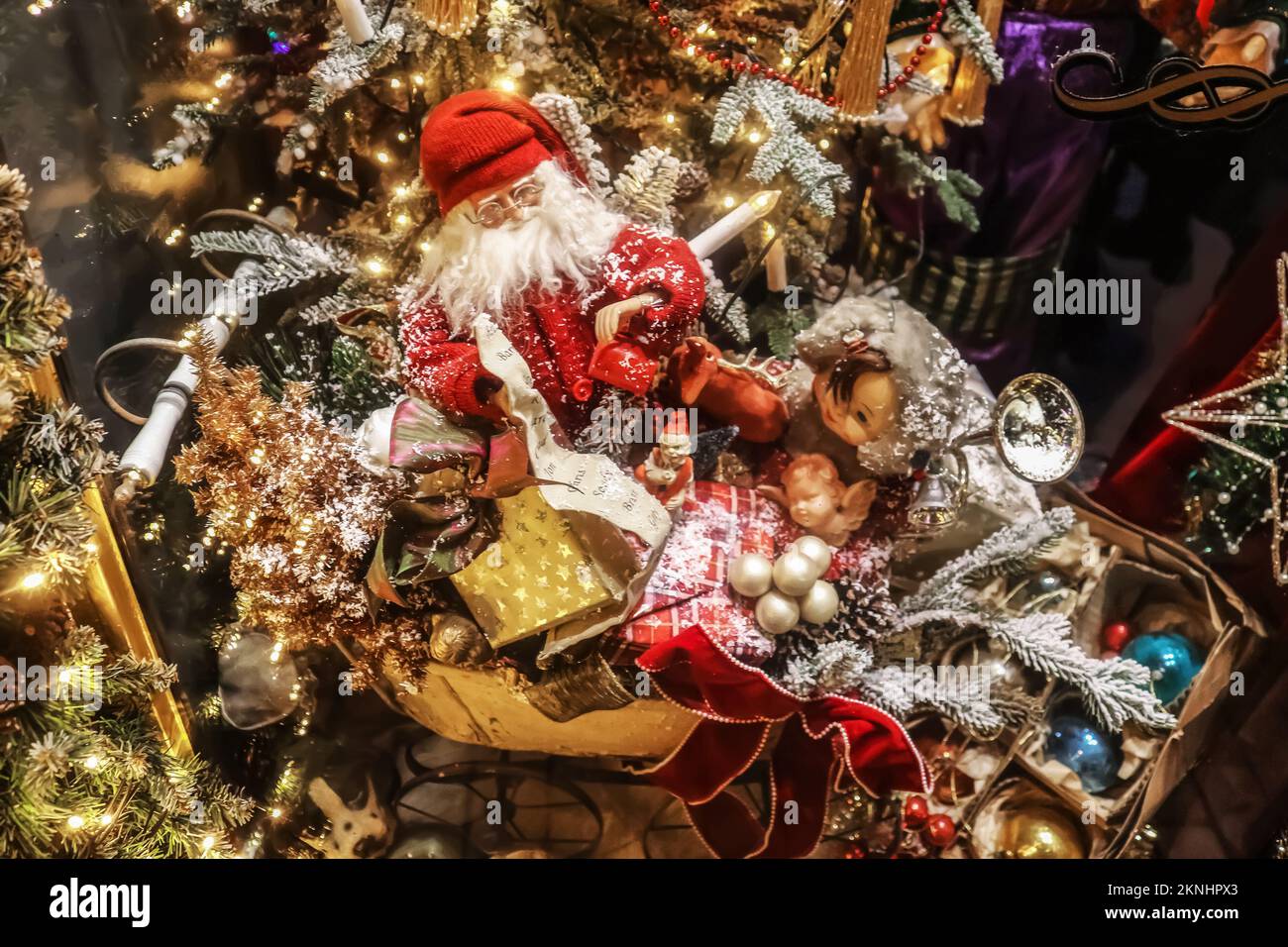Old fashioned Christmas display with santa in his sled with presents and a doll and retro Christmas ornaments in front of a tree - blurred and bokeh Stock Photo