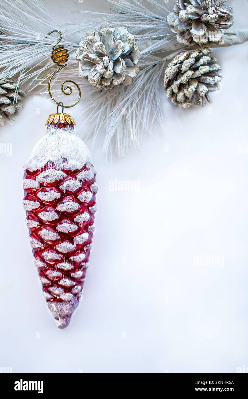 Red glass retro pine cone with snow Christmas ornament hanging from flocked branch against white background - Room for copy. Stock Photo