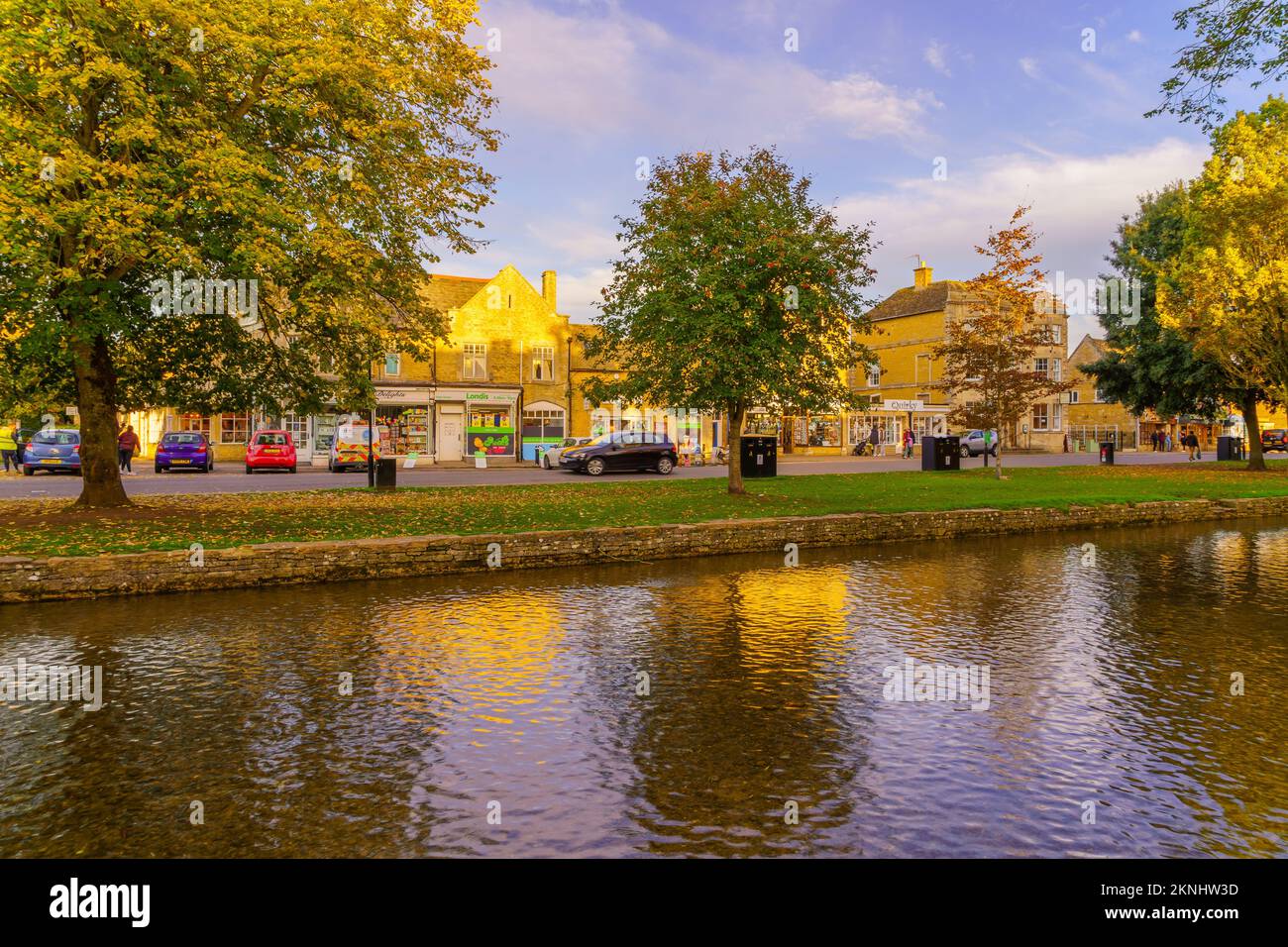 Bourton-on-the-Water, UK - October 17, 2022: Sunset scene of typical houses, the river Windrush, locals and visitors, in the village Bourton-on-the-Wa Stock Photo