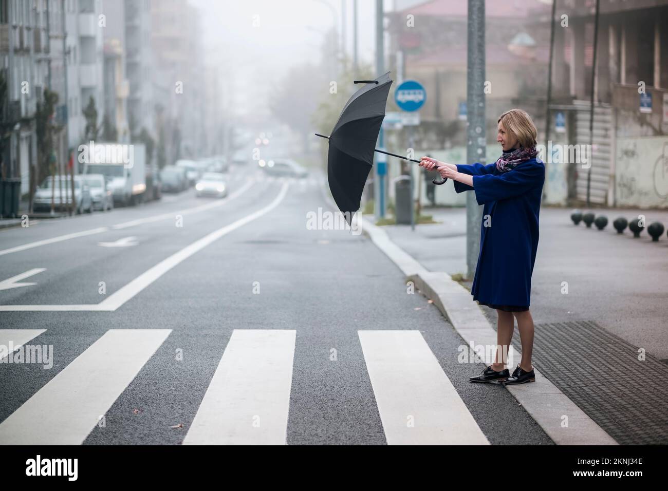 A woman opens an umbrella while crossing the road in the fog Stock ...
