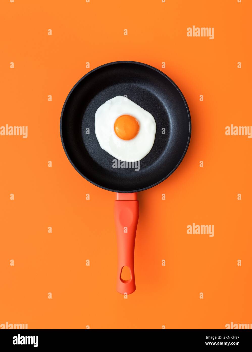 Above view with a sunny side up egg in an iron cast pan on a orange colored table. Cooking pan with a single fried egg on a colorful background. Stock Photo