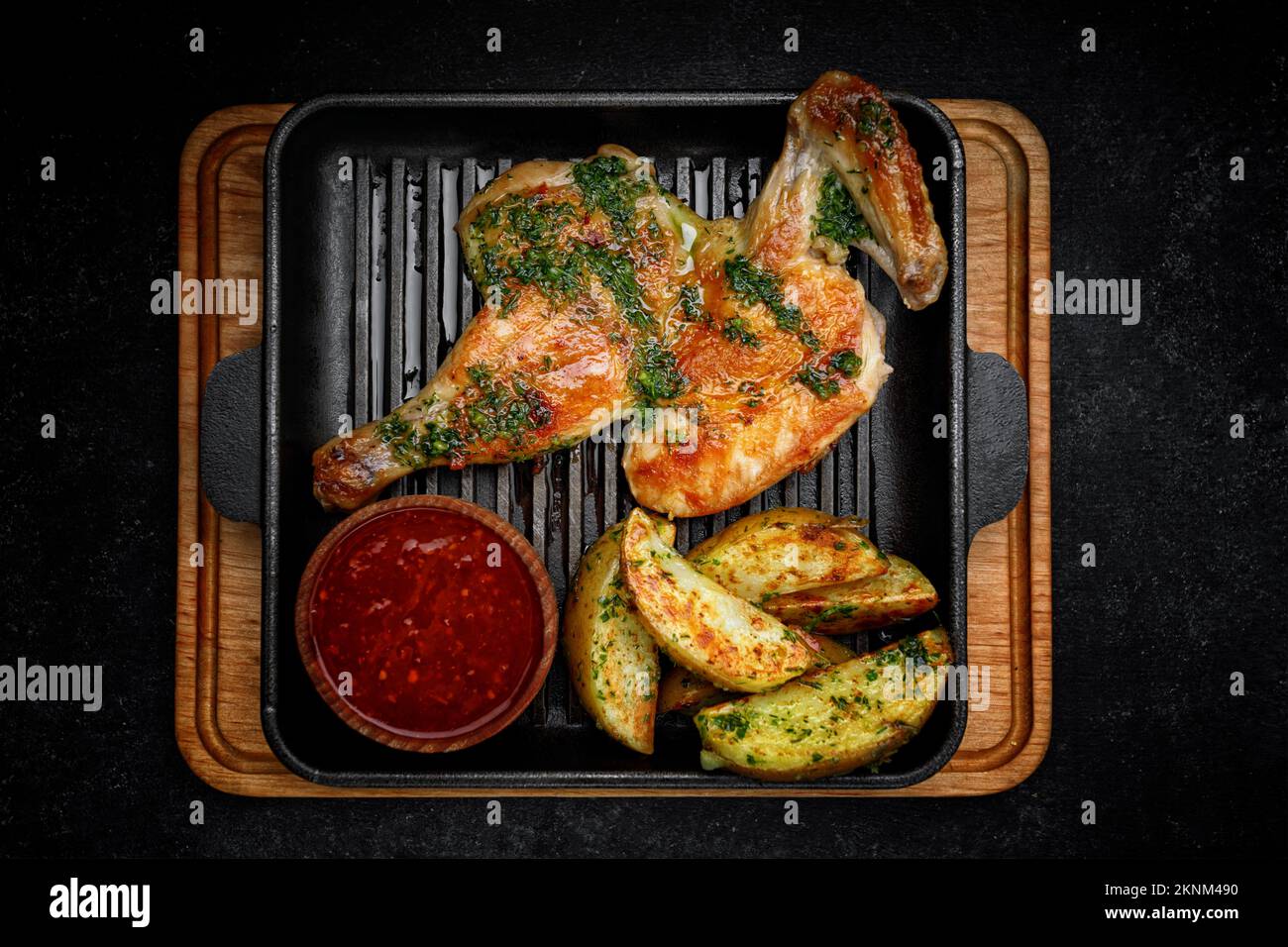 Fried half chicken with fried potatoes and spicy sauce, on a frying pan