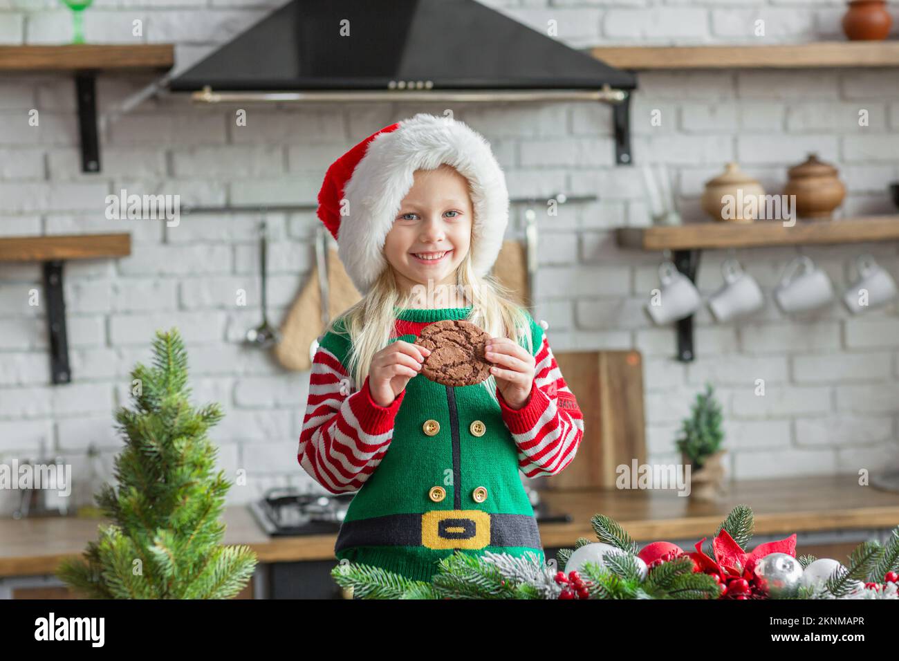 https://c8.alamy.com/comp/2KNMAPR/girl-in-santa-claus-hat-smiling-and-eating-christmas-cookie-2KNMAPR.jpg