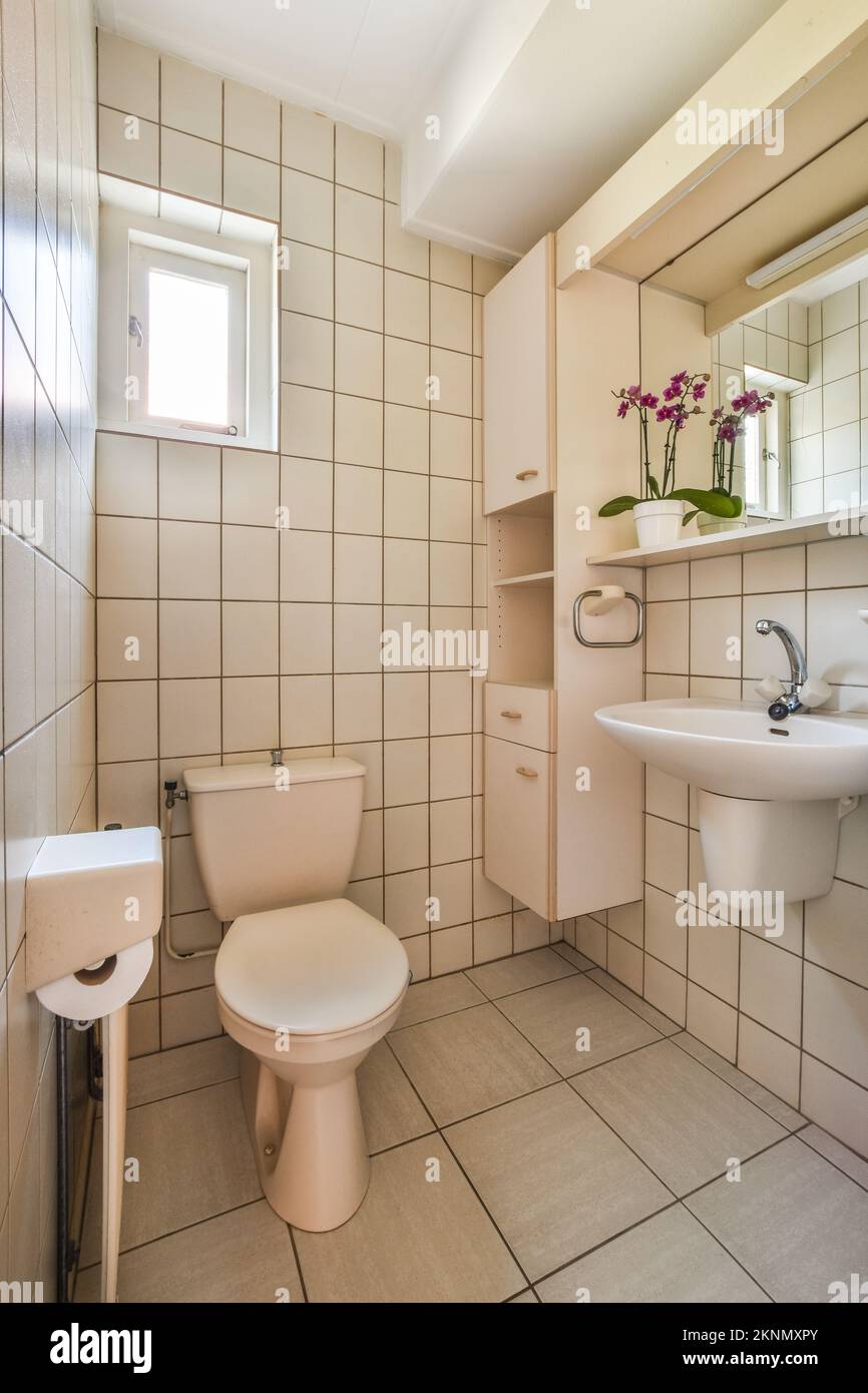 Wall hung toilet and small sink in corner in lavatory room with beige