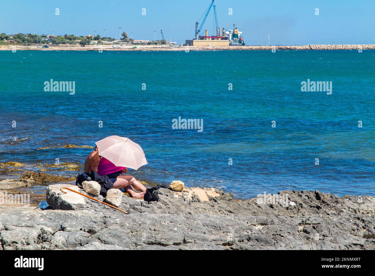 A retired couple hide from the sun under a beach umbrella in an induistrial scene Stock Photo