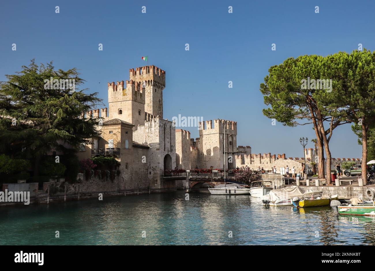 Sirmione, Italy - June 25, 2022: Scaligero Castle with Lake Garda, Small Boat and Tree. Beautiful View of Fortress in Northern Italy with Blue Sky. Stock Photo